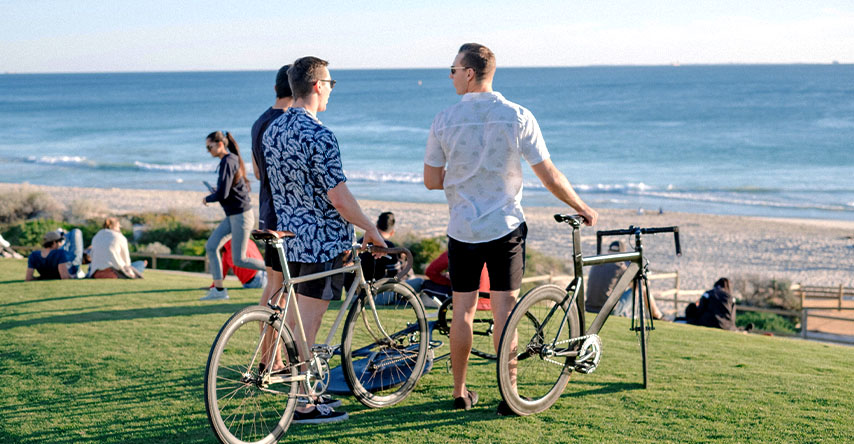 três homens com bicicletas indo à praia e conversando.