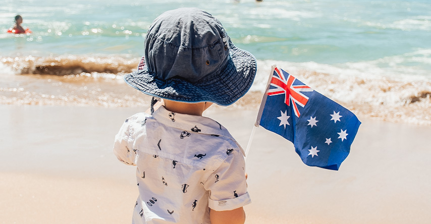 criança de costas na praia segurando a bandeira da austrália
