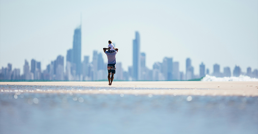 Homem caminha na praia de Gold Coast com seu filhos nos ombros